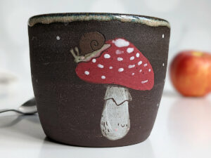 black clay cup with cute hedgehog and mushroom