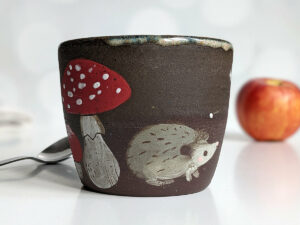 black clay cup with cute hedgehog and mushroom