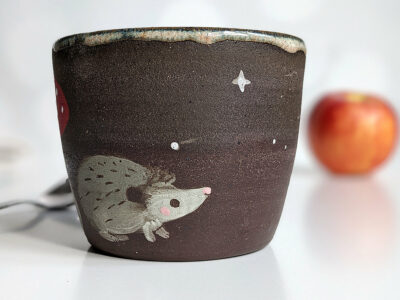 black clay cup with cute hedgehog and mushroom
